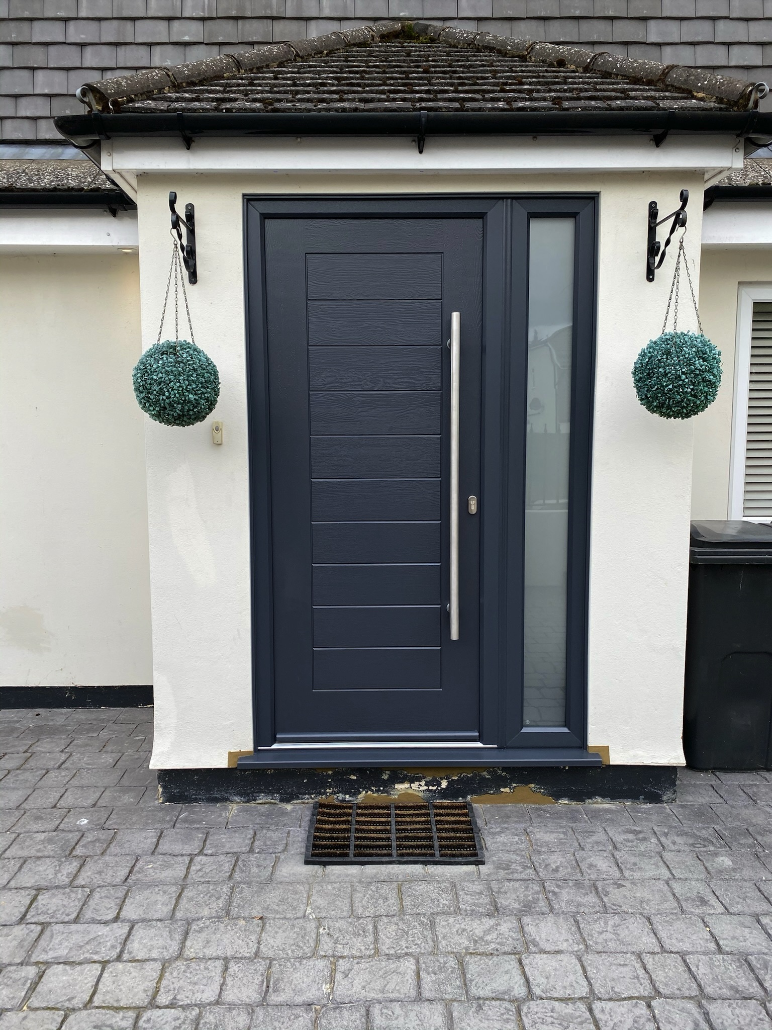 contemporary grey front door in a white render porch with silver bar handle.