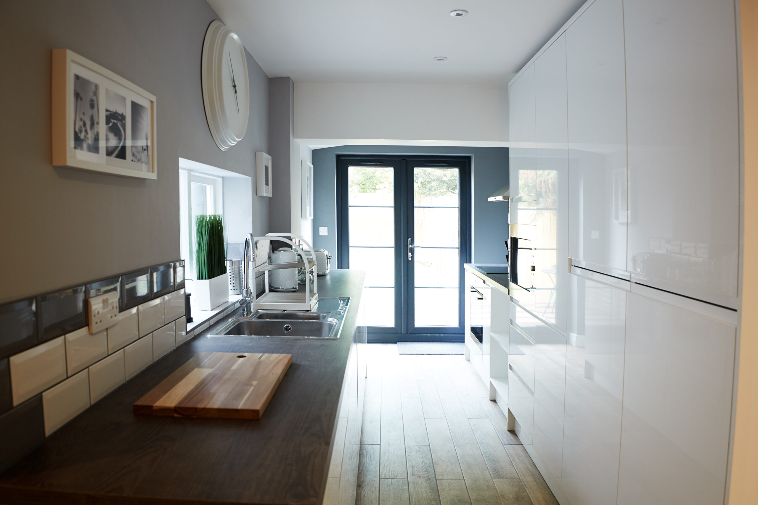 liniar french doors in a long kitchen with white units and black worktop